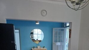 A room with wooden flooring, a round mirror on a wall, a door with glass panels, a sofa, and a table. - Triple9 Guesthouse (Hatfield, Pretoria)