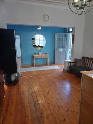 A room with wooden flooring, a round mirror on a wall, a door with glass panels, a sofa, and a table.