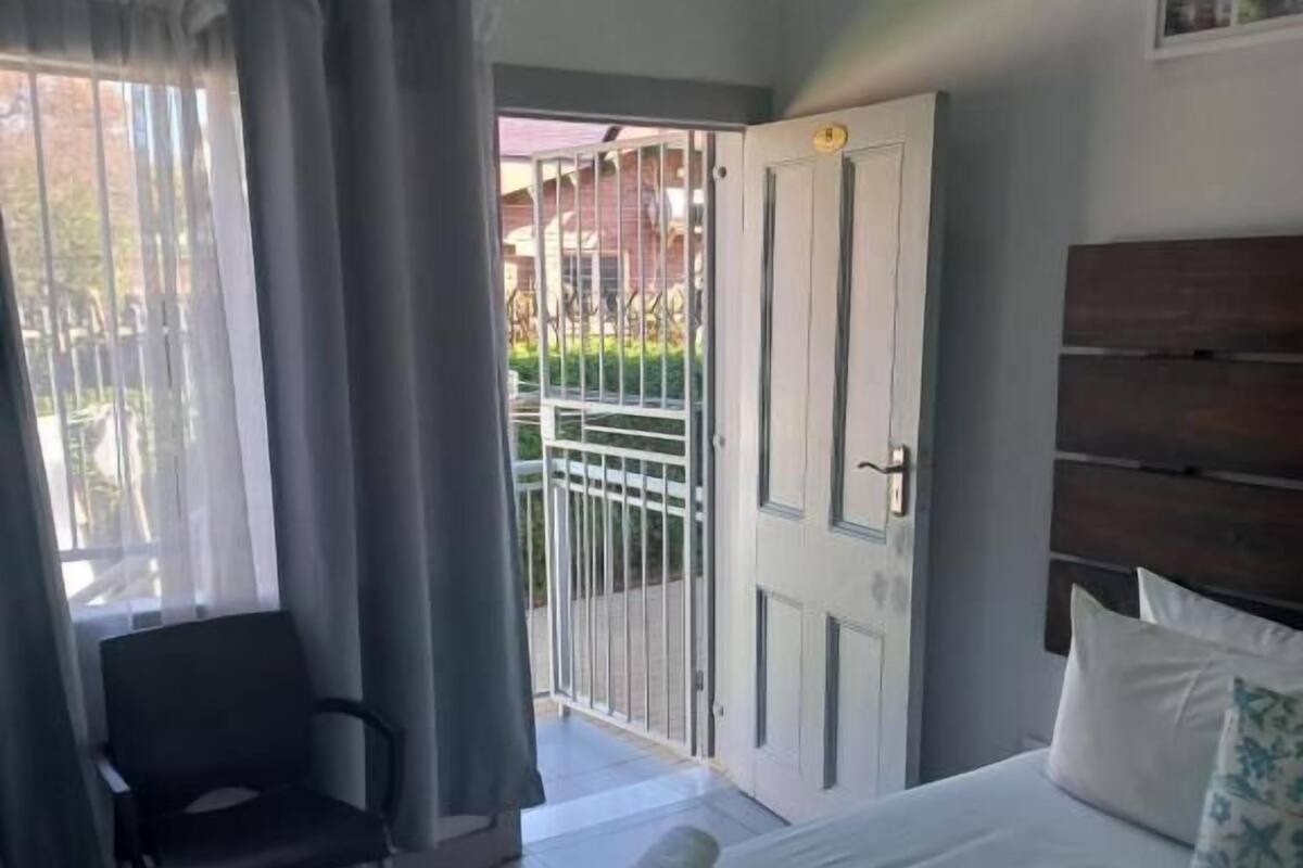 A hotel room with a bed, a chair, a door leading to a balcony, and a wooden headboard.
