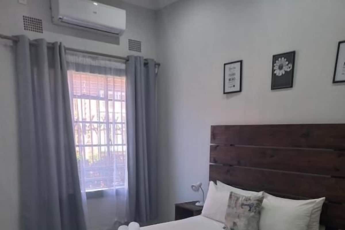 A bedroom with a bed, curtains, a nightstand, a wooden headboard, and a window with a view.