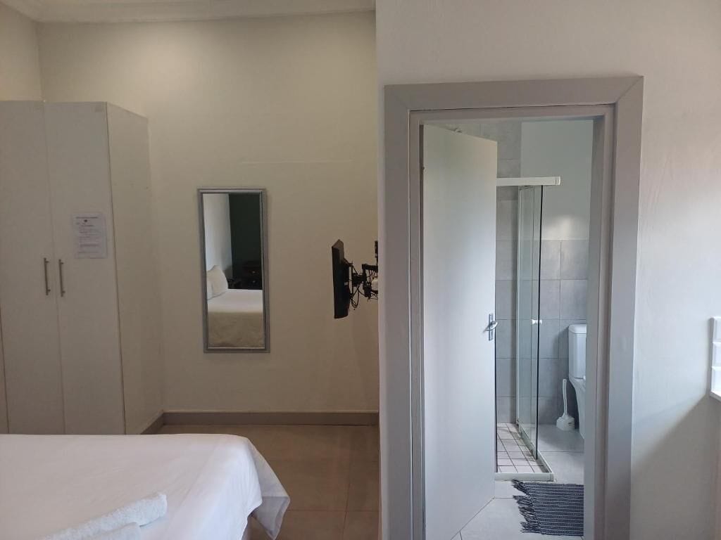 Une chambre d’hôtel comprenant un lit, une armoire, un miroir et une porte donnant sur une salle de bain avec douche et toilettes.