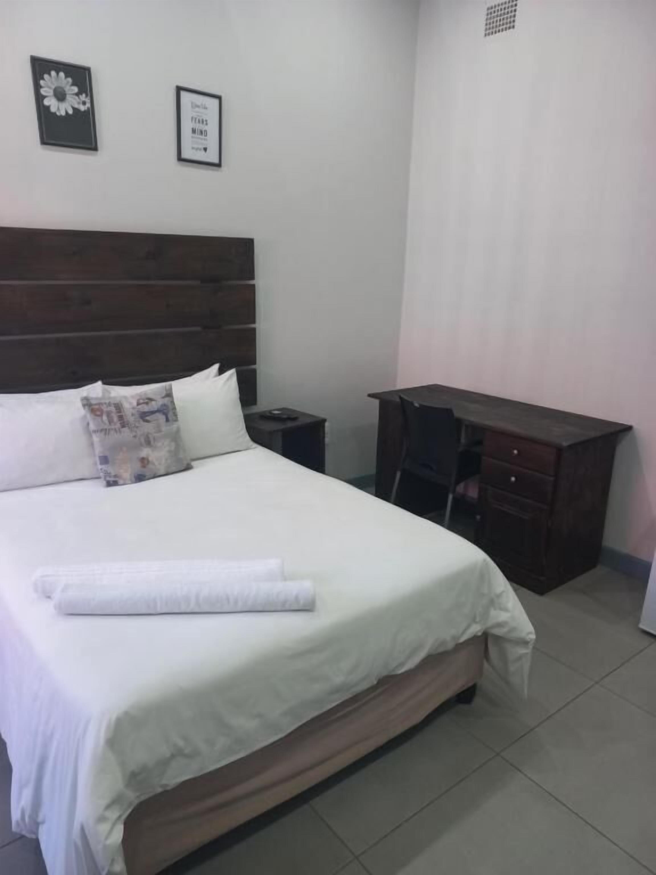 Een netjes opgemaakt bed met witte lakens, een houten hoofdbord, een nachtkastje en een donker houten dressoir.