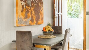 A dining area with a wooden table, four chairs, and a fruit bowl. - Rosario’s Village 2 Bed Unit 09 Bryanston (Sandton)