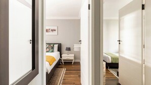 A bedroom with a bed, bedside table, lamp, and a picture on the wall. - Rosario’s Village 2 Bed Unit 09 Bryanston (Sandton)