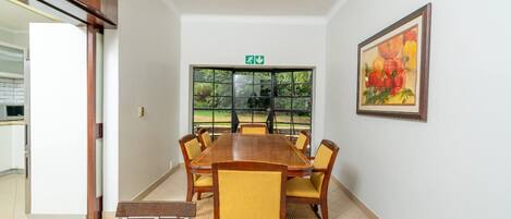 A conference room with a long table, chairs, a painting, and a window with a view of greenery.