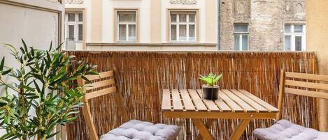 A balcony with a wooden table and two chairs, a potted plant, and a view of buildings.