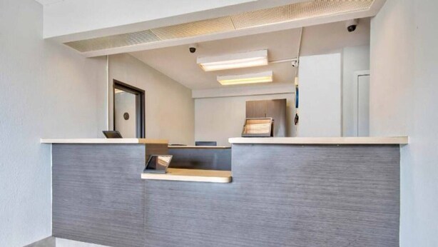 A reception desk with a grey panel, a small shelf, and a door in the background.