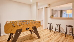 A modern room with a foosball table, wooden flooring, and three bar stools. - A Getaway in the Cotentin (Cherbourg-en-Cotentin)