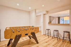 A modern room with a foosball table, wooden flooring, and three bar stools. - A Getaway in the Cotentin (Cherbourg-en-Cotentin)