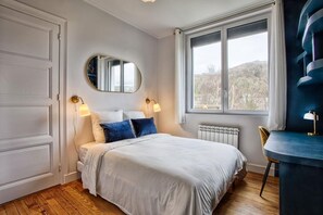 A bedroom with a bed, a window, a radiator, a chair, and a mirror. - A Getaway in the Cotentin (Cherbourg-en-Cotentin)