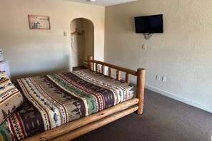 A bedroom with a wooden bed frame, a television mounted on the wall, and a small arched doorway. - Queen Bed | Murdo SD (Murdo SD)