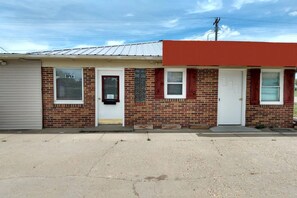A single-story brick building with a red awning, a garage door, and two windows with blinds. - Queen Bed | Murdo SD (Murdo SD)