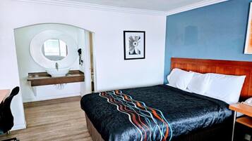 Een hotelkamer met een bed, een ronde spiegel, een wastafel, een lijst met een foto en een houten hoofdeinde.