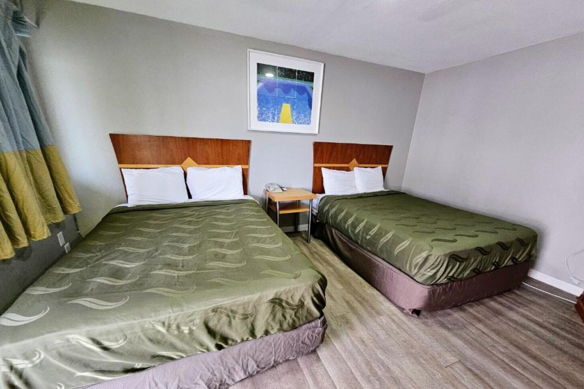 Habitación de hotel con dos camas individuales, una mesita pequeña y un cuadro en la pared.
