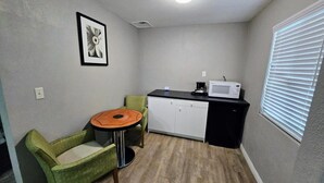 A small kitchenette with a microwave, a coffee maker, and a cabinet. There is a small dining table with a chair. - King Bed|Non-Smoking (Ridgecrest CA)