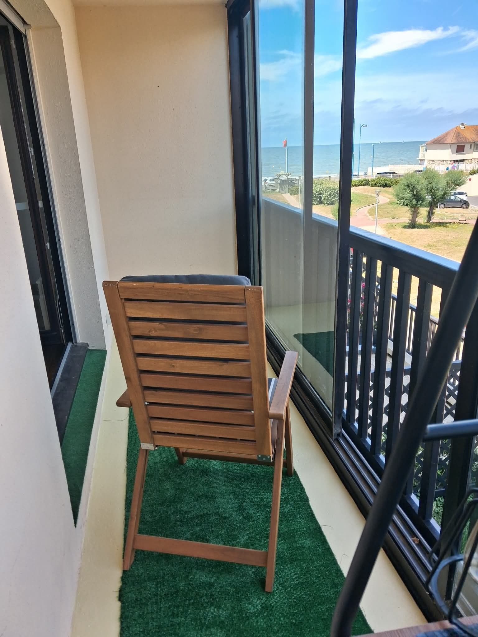 Une chaise en bois sur un balcon, avec vue sur la mer et un bâtiment visible au loin.