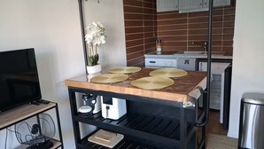 Eine Küche mit Holzarbeitsplatte, einem schwarzen Metallregal, einem Topfpflanzen und einem Fernseher auf einem Standfuß.