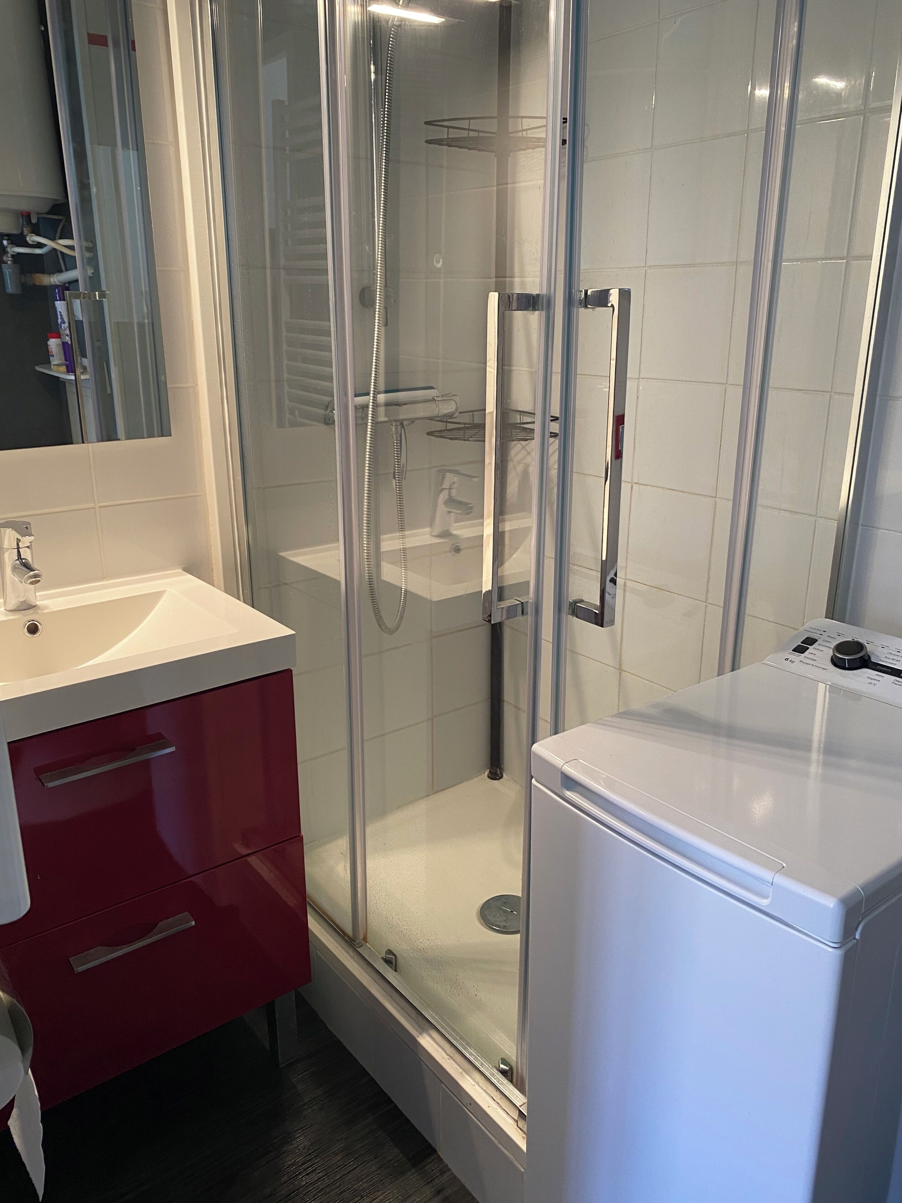 Een moderne badkamer met een glazen douchecabine, een wit wastafelmeubel en een rode kast.