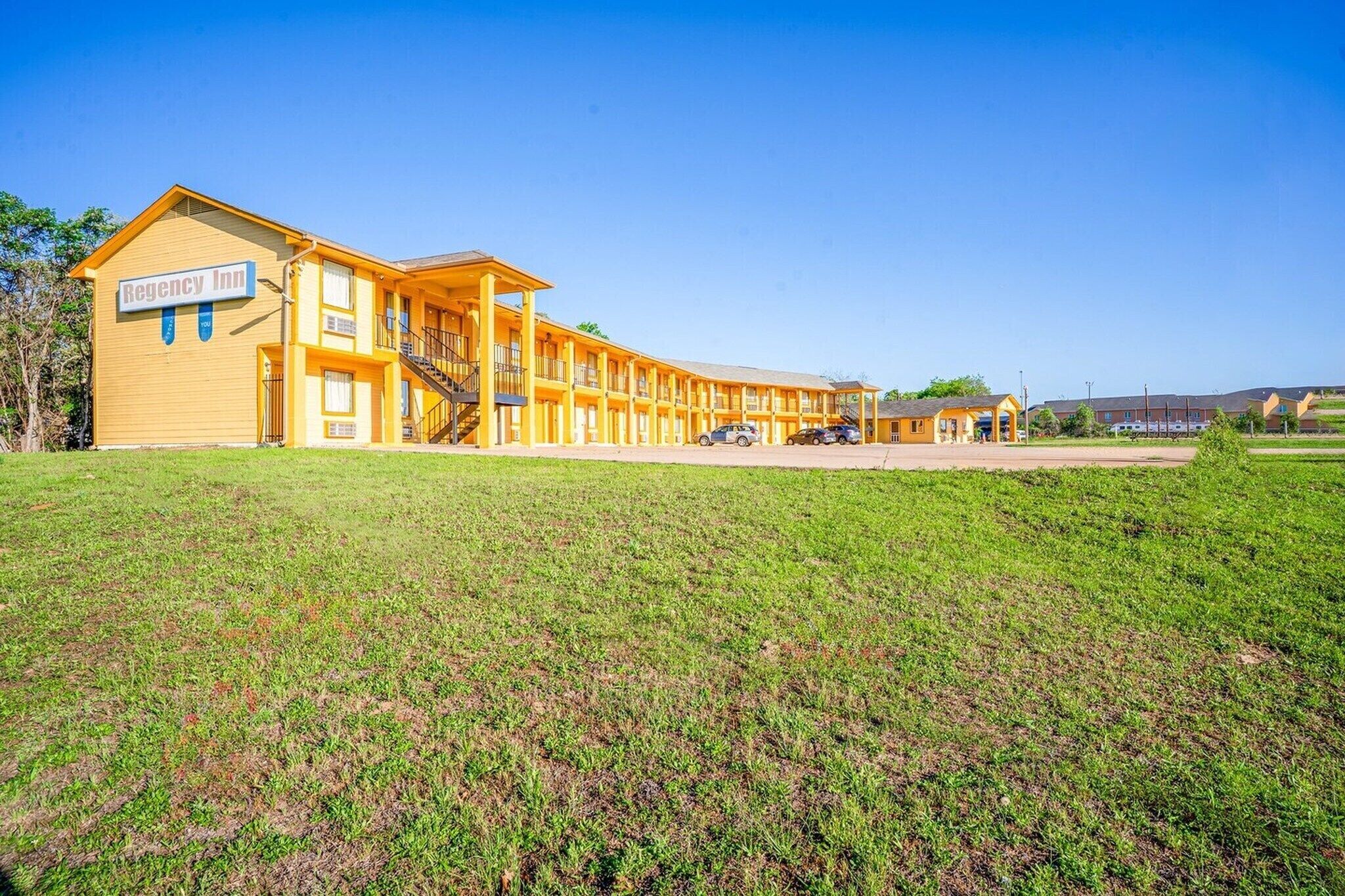 A motel with a yellow exterior, multiple balconies, and a sign reading 'Regency Inn.'