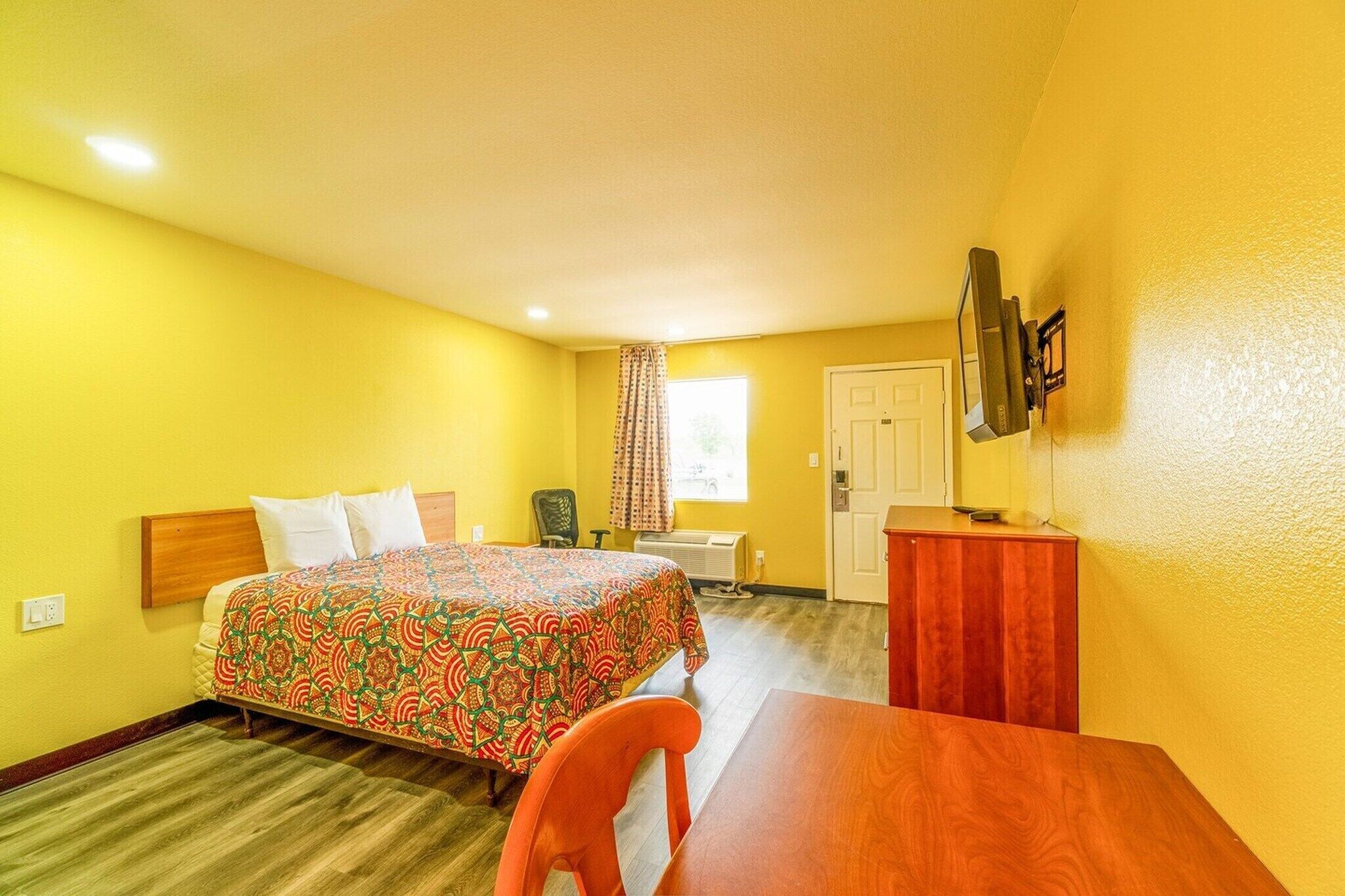 Una habitación de hotel con cama, escritorio, silla, televisor y ventana con cortinas.