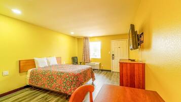 Una habitación de hotel con cama, escritorio, silla, televisor y ventana con cortinas.