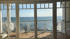 A room with a large sliding glass door leading to a wooden deck with a view of the ocean and a bridge. - "Prinz Heinrich" Ocean View Villa - Molenblick Apartment (Sassnitz)