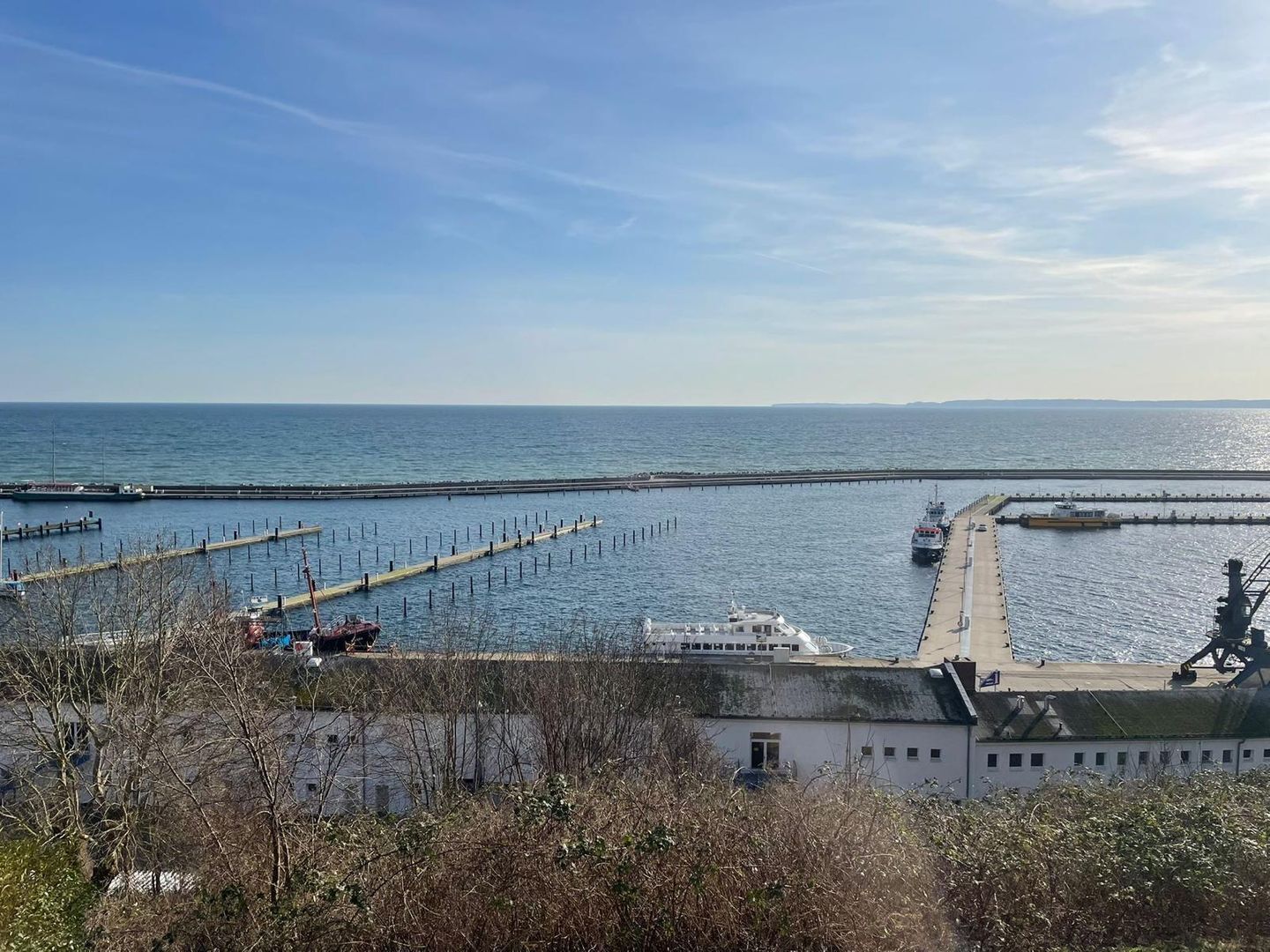 Blick auf die Küste mit einem Steg, der ins Meer führt, ein Boot an Deck und ein Gebäude mit Gründach im Vordergrund.