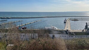 A coastal view with a pier extending into the sea, a boat docked at the pier, and a building with a green roof in the foreground. - "Prinz Heinrich" Ocean View Villa - Molenblick Apartment (Sassnitz)