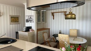 A kitchen with a modern stove, a dining area with a table and chairs, and a hanging light fixture. - "Prinz Heinrich" Ocean View Villa - Molenblick Apartment (Sassnitz)