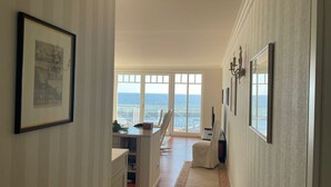 A hallway with a view of the ocean, framed artwork, and a seating area with a chair. - "Prinz Heinrich" Ocean View Villa - Molenblick Apartment (Sassnitz)