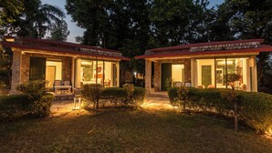 Two small, stone buildings with glass doors and windows, surrounded by well-maintained bushes and grass. - The Roar Resort (Ramnagar)