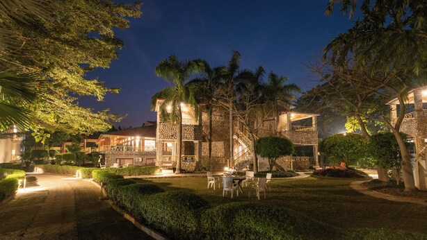 A well-lit outdoor area with stone buildings, palm trees, and a paved walkway. - The Roar Resort (Ramnagar)