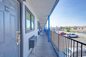 Un balcón con barandal azul, una puerta con el número 212 y vista a un estacionamiento con coches.