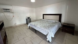 Ein Schlafzimmer mit Bett, Nachttisch, kleinem Schreibtisch und Klimaanlage.