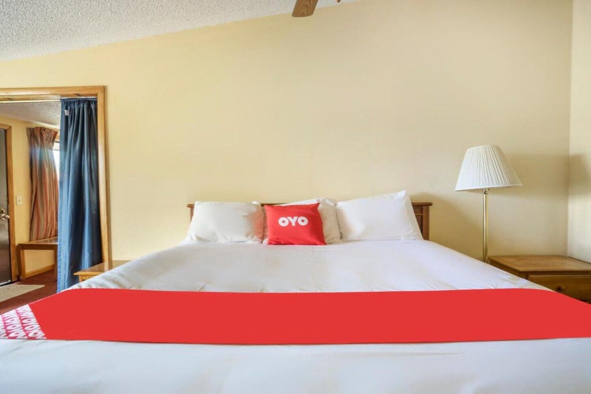 Habitación de hotel con cama, mesita de noche, lámpara y puerta con cortinas.