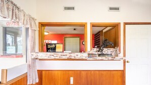 Un espace d’accueil comprenant un comptoir, un lambris en bois, une porte et une vue sur une pièce dont le mur est rouge et où l’on aperçoit une horloge.