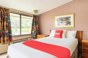 Habitación de hotel con una cama grande, una mesita de noche, un cuadro en la pared y una ventana con cortinas.