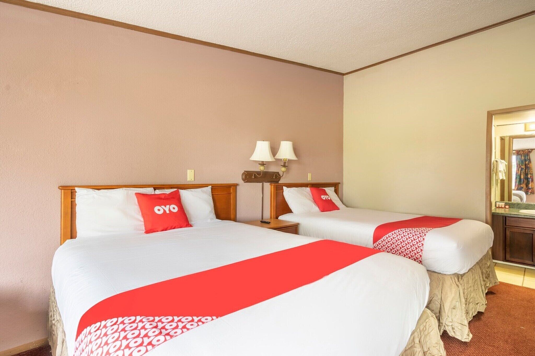 Une chambre d’hôtel avec deux lits, chacun agrémenté de draps blancs et de touches de couleur rouge, une table de chevet avec une lampe et un miroir au mur.
