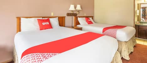 Habitación de hotel con dos camas, cada una con ropa blanca y detalles rojos, una mesita de noche con lámpara, y un espejo en la pared.