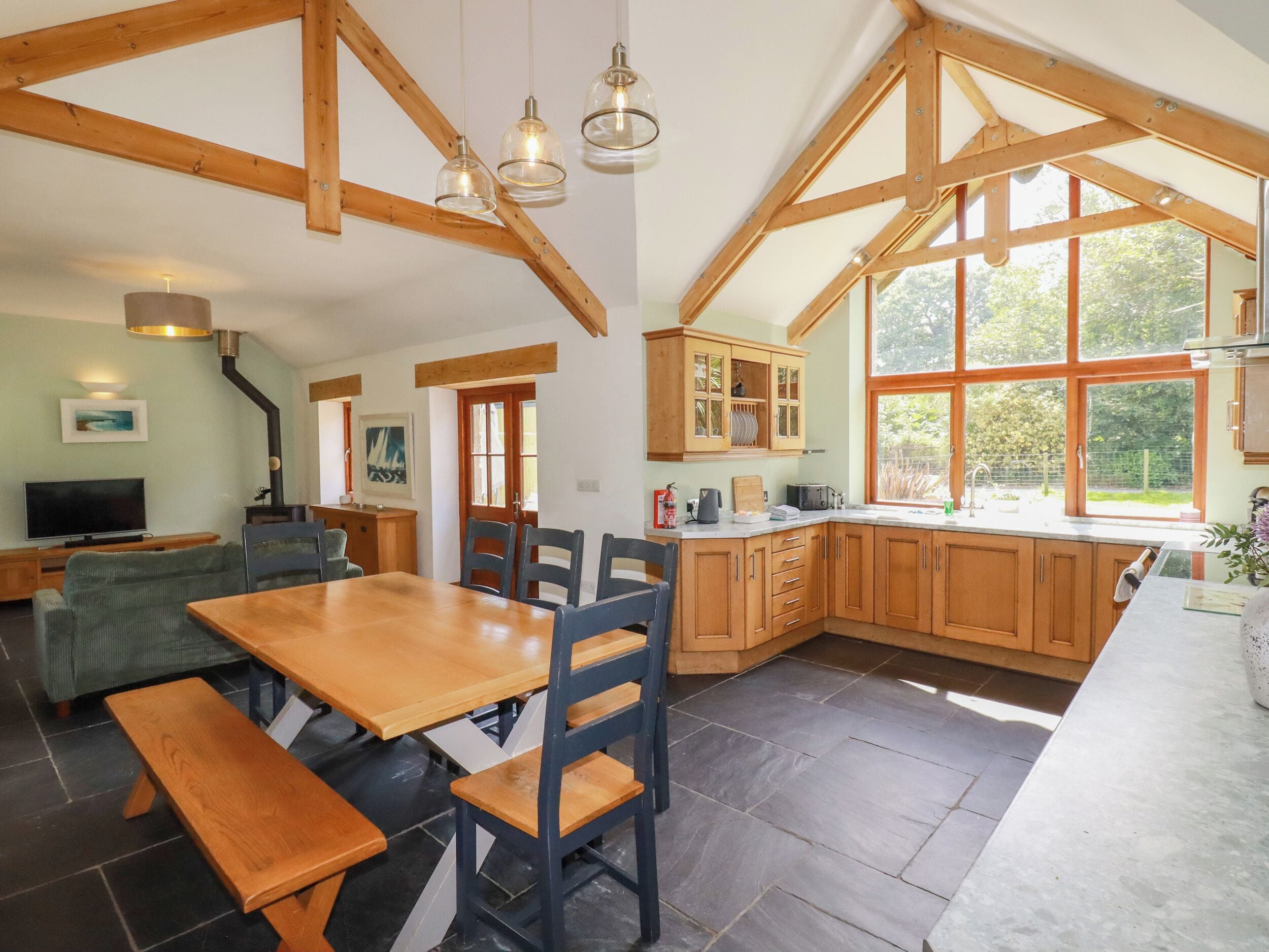 A spacious kitchen with wooden beams, a dining area with a wooden table and chairs, and a large window providing natural light.