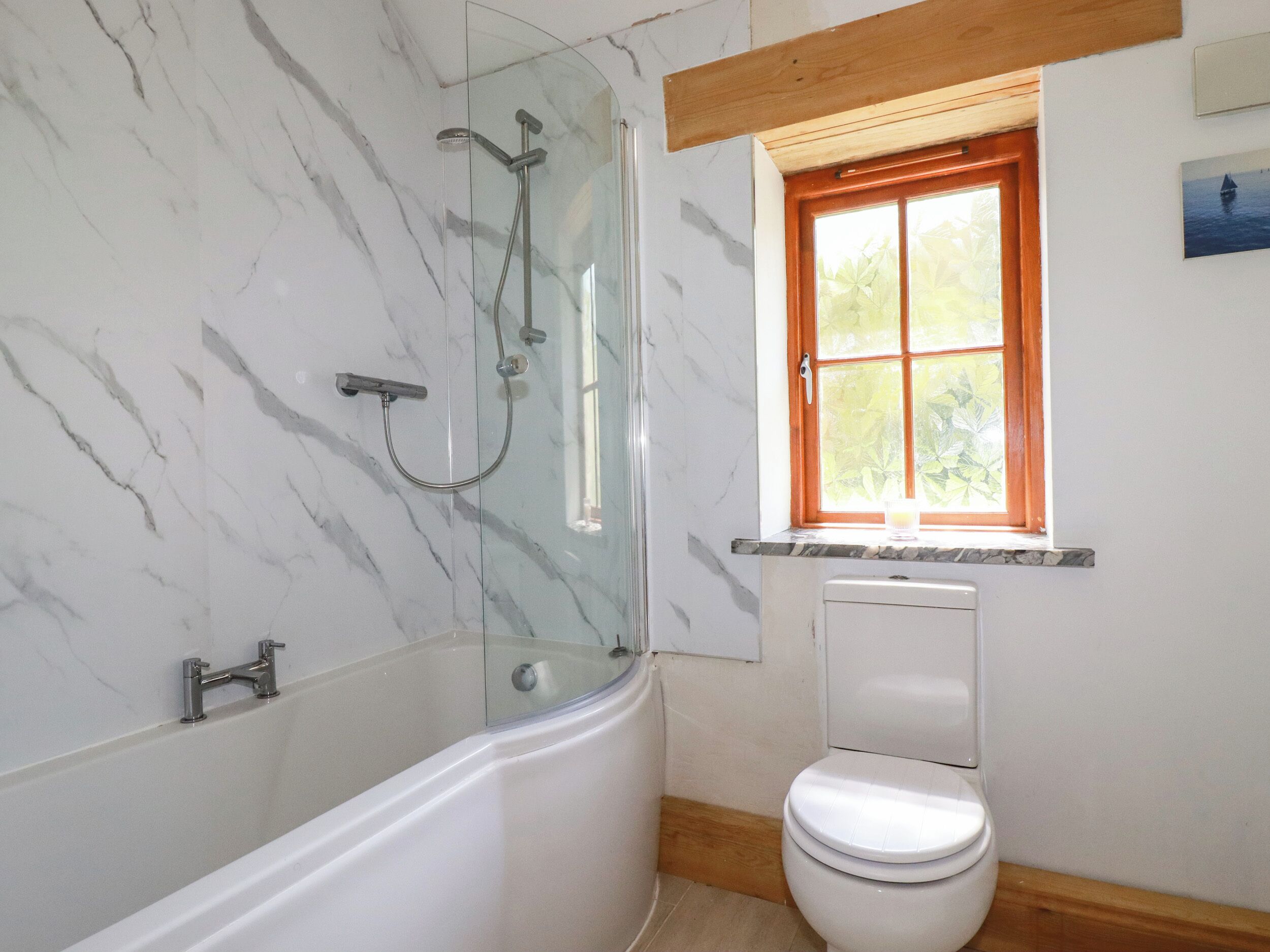 A bathroom with a glass-enclosed shower, a toilet, and a window with a view of greenery.