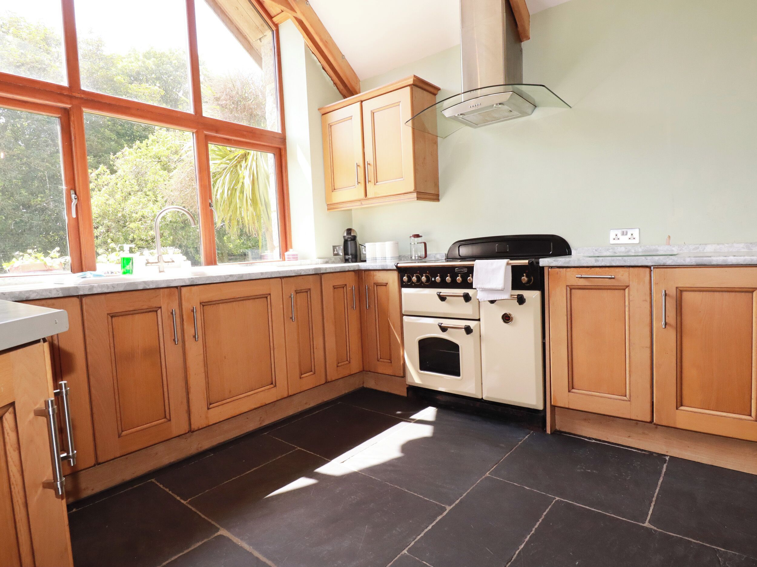 A kitchen with wooden cabinets, a stove, and a window with a view of greenery.