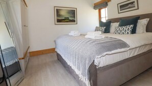 A bedroom with a bed, a nightstand, a wardrobe, and two framed pictures on the wall. - Little Trethellan (Redruth)