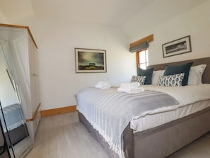 A bedroom with a bed, a nightstand, a wardrobe, and two framed pictures on the wall. - Little Trethellan (Redruth)