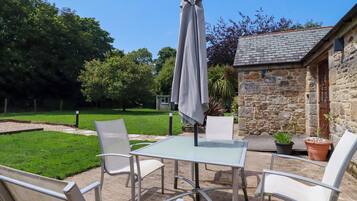 Eine Terrasse mit Tisch und Stühlen, einem Sonnenschirm und einem Gebäude im Hintergrund.