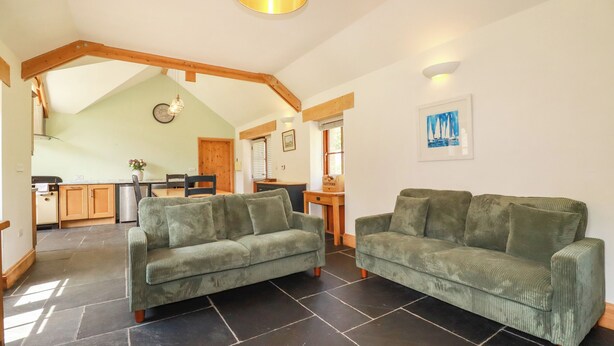 A spacious living area with two green sofas, a kitchen in the background, and a dining area. - Little Trethellan (Redruth)