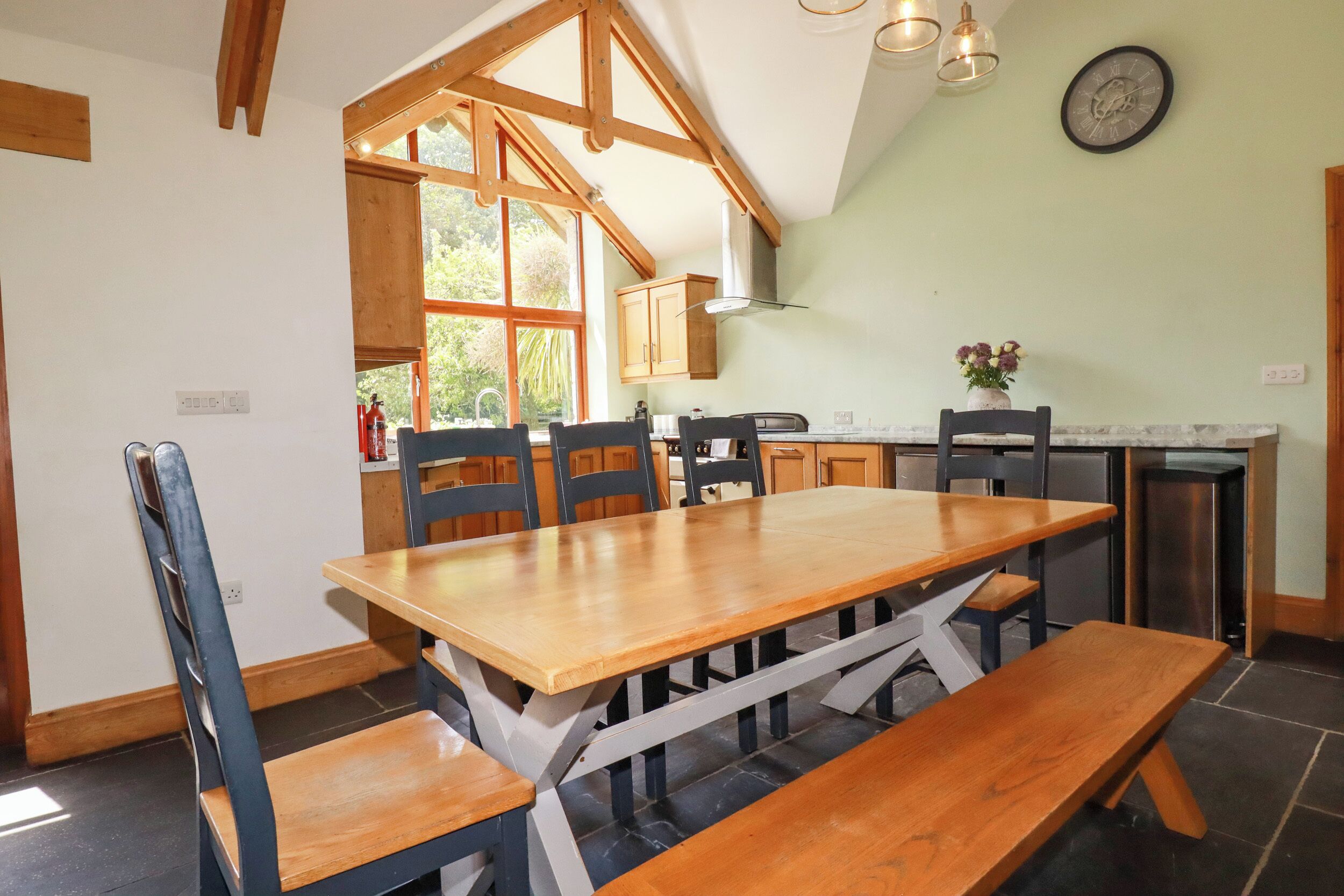 A dining area with a wooden table and benches, a kitchen with wooden cabinets, and a large window.