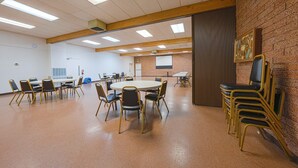 Un salón de conferencias con mesas y sillas redondas, una pared de ladrillo y un ventanal grande.