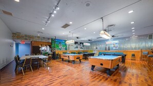 Sala de billar con mesas de billar, sillas y zona de bar.