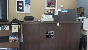 A reception desk with a sign indicating check-out time, a computer, and a framed picture on the wall.